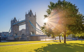 London, Großbritannien – berühmte Tower Bridge bei Sonnenaufgang mit Sonnenlicht, Bäumen, blauem Himmel und grünem Gras
